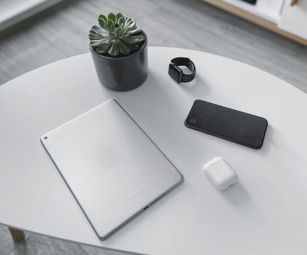 Elegantes Tech-Setup mit Tablet, Smartphone, Smartwatch und kabellosen Kopfhörern auf einem weißen Tisch – minimalistisches Design für modernes Arbeiten.